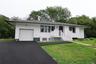 White exterior siding with dark trim, attached garage, front porch with white railing, paved driveway, and grass lawn