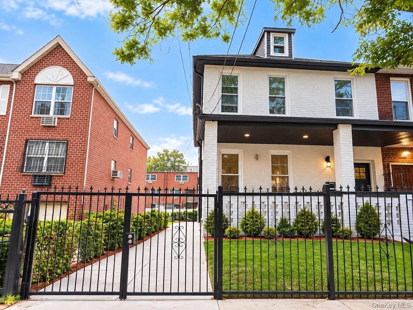 White brick exterior with black trim, covered porch with recessed lighting, dormer window, wrought iron fencing, and established front landscaping