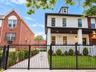 White brick exterior with black trim, covered porch with recessed lighting, dormer window, wrought iron fencing, and established front landscaping