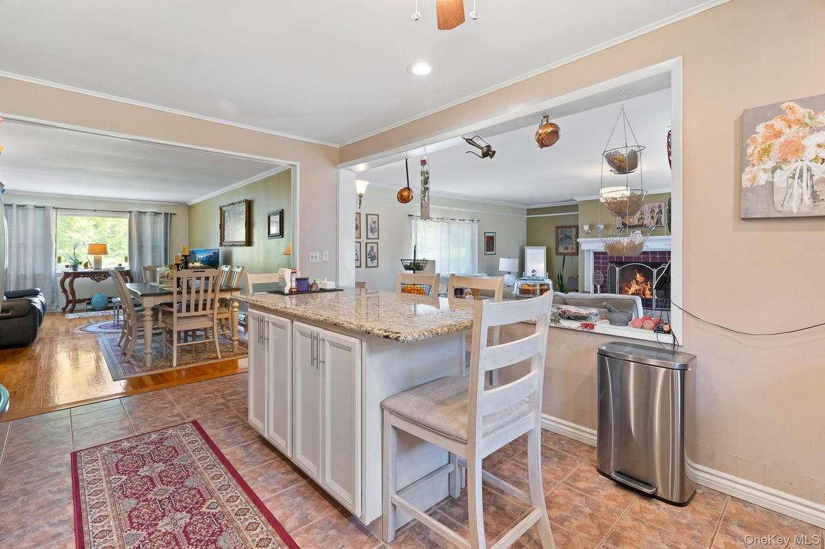 Kitchen with open floor plan, ornamental molding, white cabinets, a brick fireplace, and light stone counters