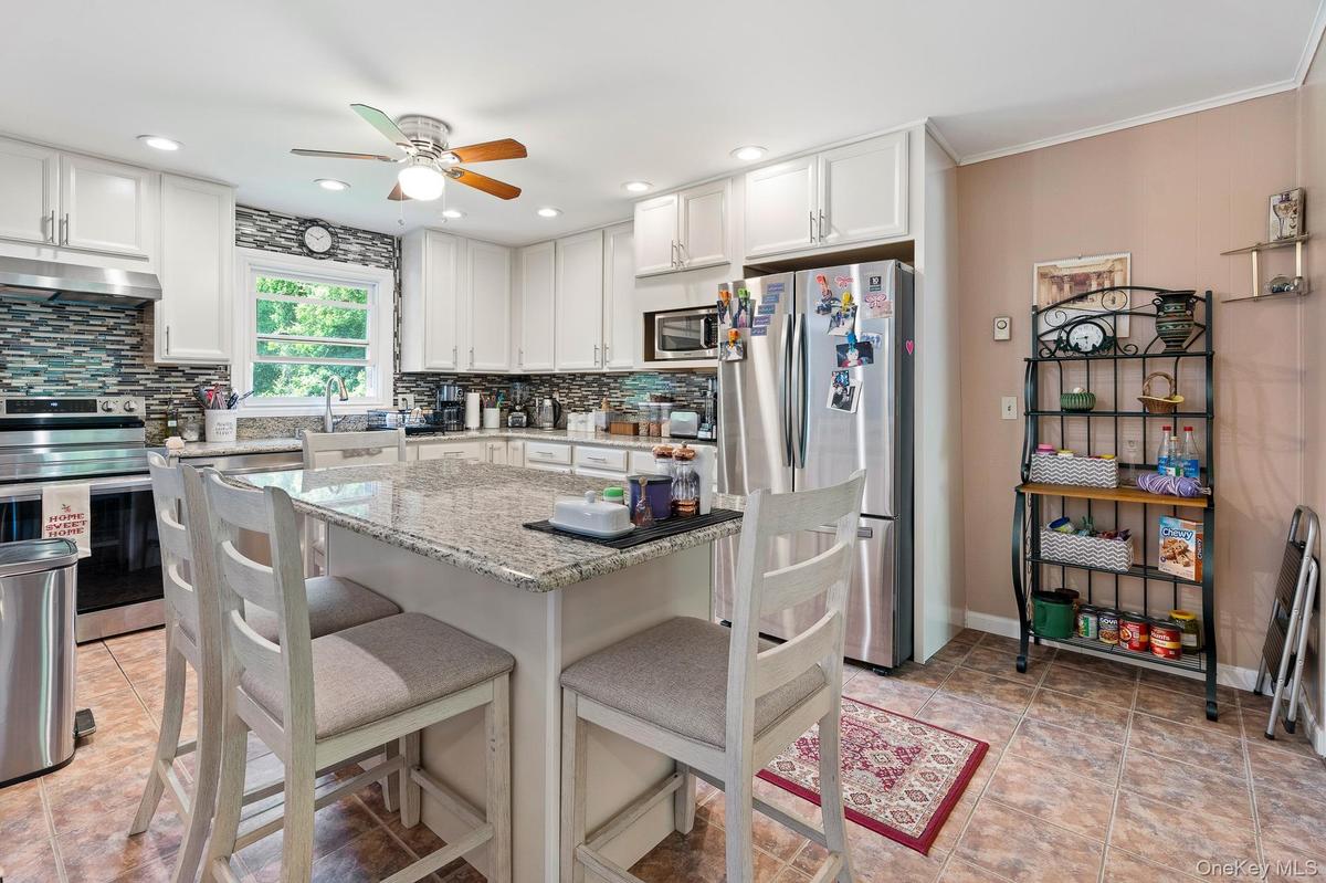Kitchen featuring appliances with stainless steel finishes, under cabinet range hood, ceiling fan, tasteful backsplash, and a breakfast bar area