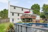Two-story exterior with white siding, elevated wood deck with railing, ground-level screened door, and an above-ground swimming pool