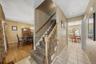 Hallway with square tile flooring, staircase with carpeted treads and wood banister, and wood-finish flooring in an adjoining room