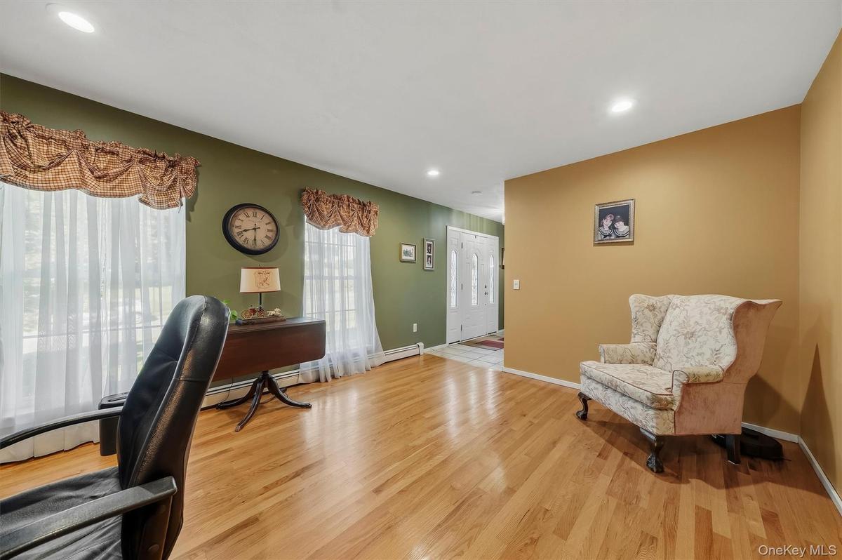 Spacious home office featuring warm wood-finish flooring, dual windows with decorative valances and sheer panels, green accent wall with wall-mounted 