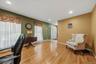 Spacious home office featuring warm wood-finish flooring, dual windows with decorative valances and sheer panels, green accent wall with wall-mounted 