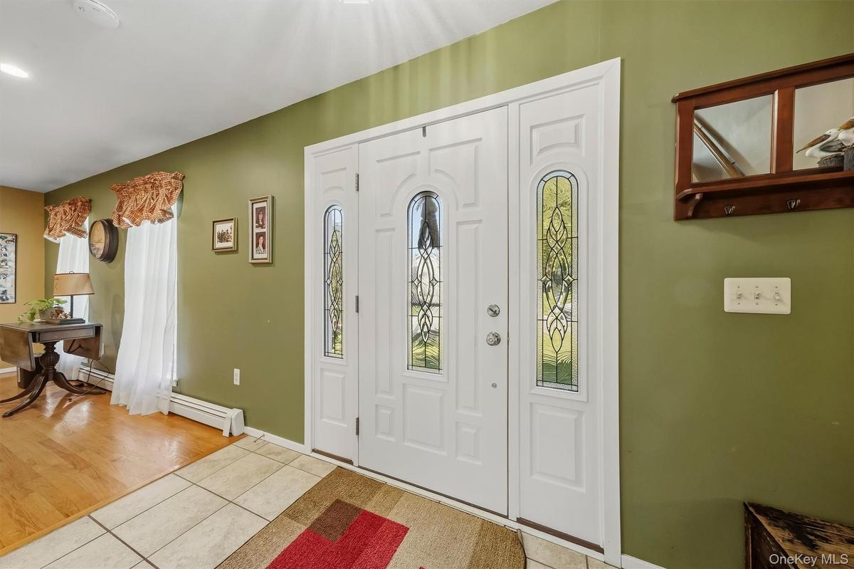 Entryway featuring a white double door with decorative glass inserts, ceramic tile flooring, and wood-finish flooring