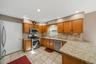 Kitchen featuring tile flooring, wood-finish cabinetry, stone countertops, and stainless steel appliances