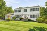 White siding exterior with dark shutters, attached two-car garage, established front landscaping, and a paved driveway