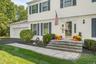 Welcoming front elevation featuring a two-story Colonial design with white horizontal siding, multi-pane windows, and a covered entry portico with sto