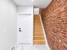 Exposed brick accent wall, wood staircase with white risers, white panel door with matte black hardware, recessed ceiling lighting, and white tile flo