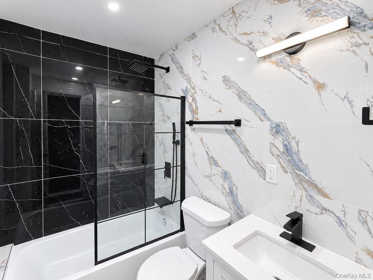 Bathtub with black-framed glass shower enclosure, black tiled shower surround, patterned wall tile, contemporary vanity with integrated sink, and matt
