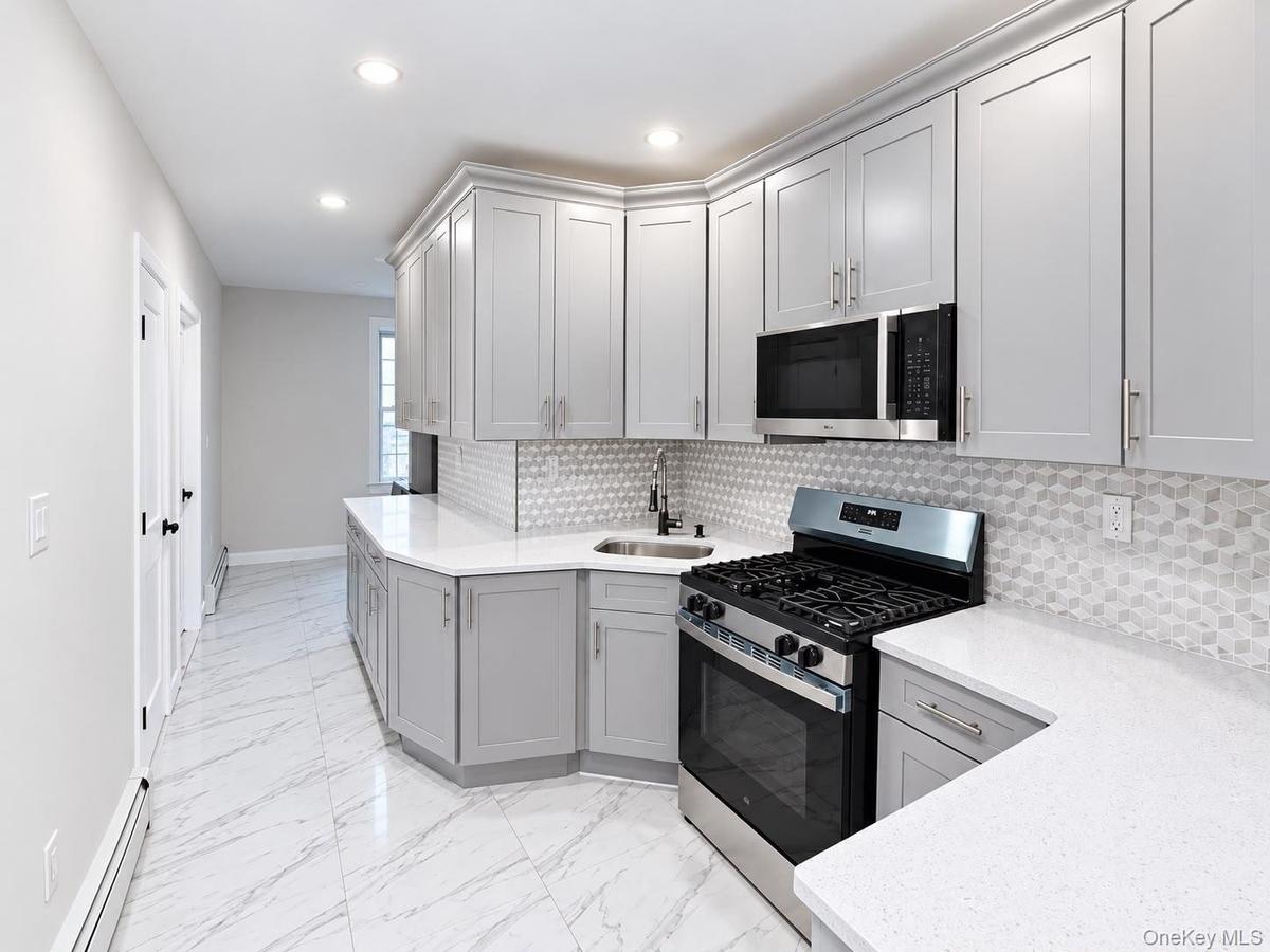 Kitchen featuring light gray cabinetry, white countertops, stainless steel appliances, geometric tile backsplash, and recessed lighting