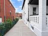 Concrete walkway with a chain-link fence, brick exterior, and a porch with a decorative railing