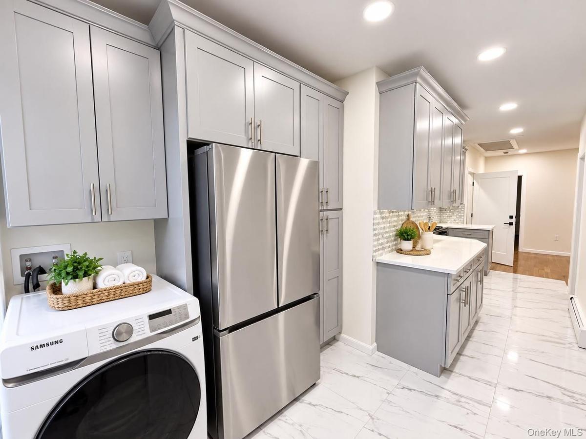 Expansive kitchen featuring light gray cabinetry, stainless steel appliances, white countertops, a tiled backsplash, and large format floor tiles