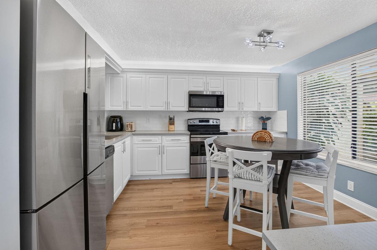 Kitchen featuring white shaker cabinetry, stainless steel appliances, wood-finish flooring, and a white subway tile backsplash