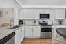 White shaker-style cabinetry, stainless steel appliances, quartz countertops, subway tile backsplash, and wood-finish flooring