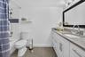 White bath vanity with a grey countertop, framed mirror, and tile flooring