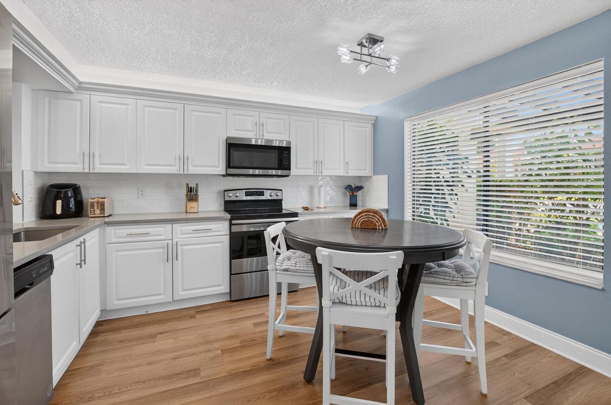 Modern kitchen featuring white shaker cabinetry, stainless steel appliances, wood-finish flooring, and sunlight!