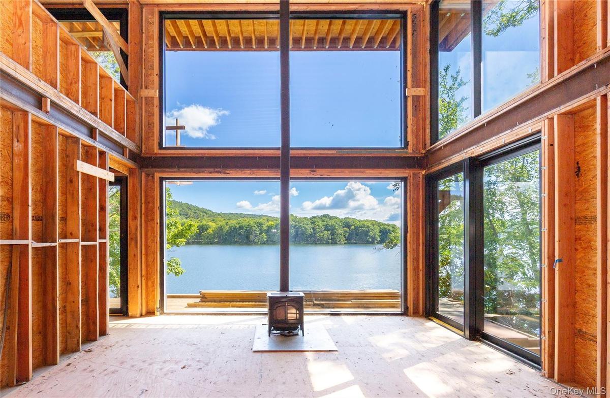 Inside, the main level is defined by a centered wood-burning stove that aligns with the window mullions, creating the illusion of one unbroken wall of