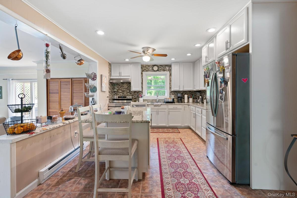 Kitchen featuring stainless steel appliances, a ceiling fan, a baseboard heating unit, decorative backsplash, and white cabinetry