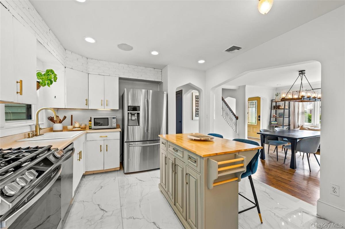 White cabinetry with gold-finish hardware, stainless steel appliances, a center island with a wood-finish countertop, marble-look floor tile, and an a