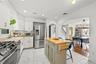 White cabinetry with gold-finish hardware, stainless steel appliances, a center island with a wood-finish countertop, marble-look floor tile, and an a