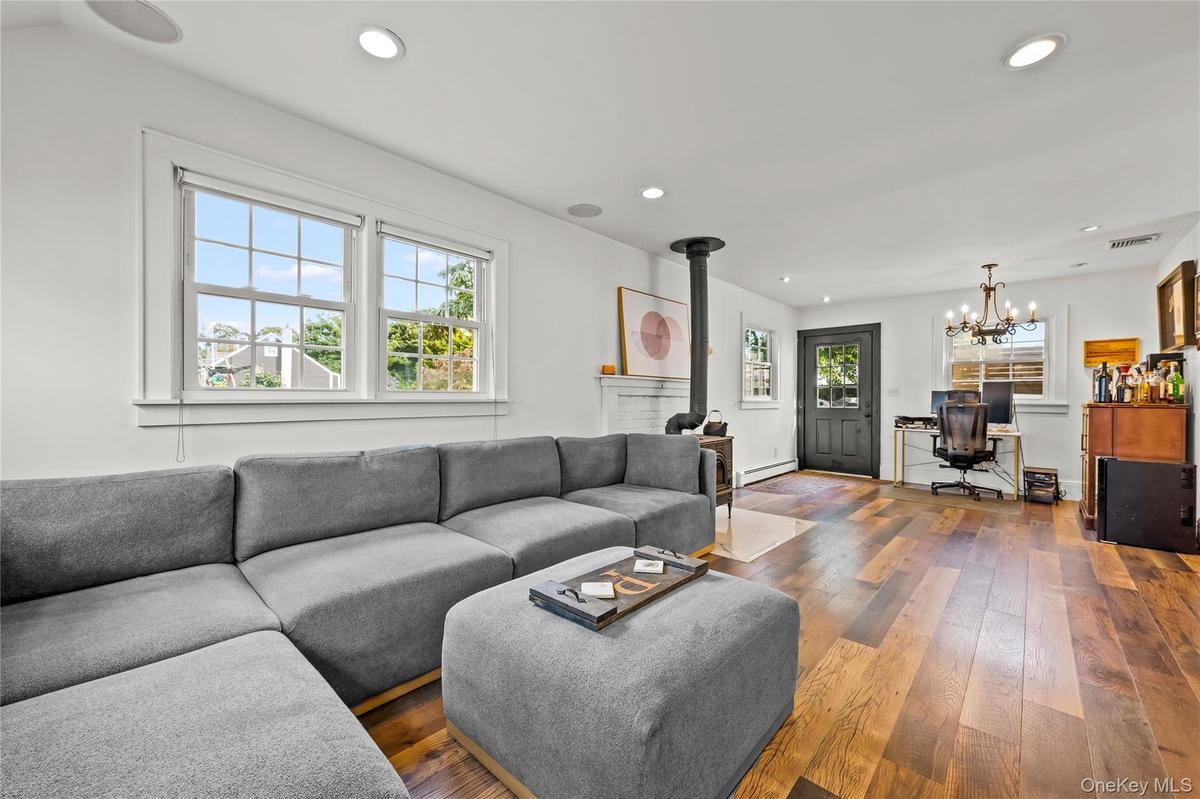 Wood-finish flooring, recessed ceiling lighting, a wood-burning stove with a decorative mantle, and white trim windows