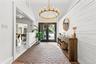 Brick flooring, vaulted white ceiling, shiplap wall, brass chandelier, and double entry doors
