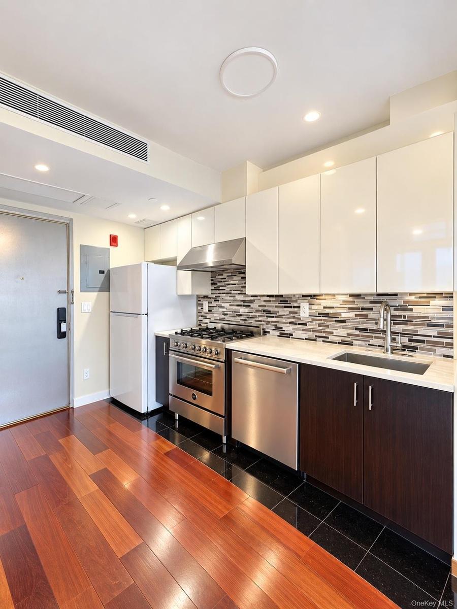 Gleaming wood-finish flooring, stainless steel appliances, white flat-panel cabinetry, a mosaic tile backsplash, and a light-toned countertop