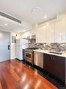 Gleaming wood-finish flooring, stainless steel appliances, white flat-panel cabinetry, a mosaic tile backsplash, and a light-toned countertop