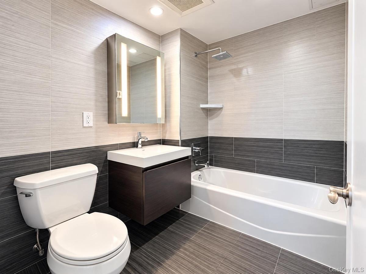 Modern bathroom featuring a floating vanity with integrated sink, illuminated medicine cabinet, rainfall shower head, and two-tone tile walls