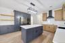 Kitchen featuring wall chimney exhaust hood, light wood-type flooring, pendant lighting, a kitchen island, and black appliances