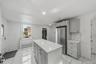 Kitchen featuring a central island with countertop, stainless steel refrigerator, light gray cabinetry, subway tile backsplash, and white tile floorin