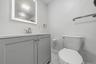 Lighted vanity mirror, gray vanity with cabinet storage, white countertop, modern brushed nickel faucet, and white tile flooring