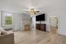 Light wood-finish flooring, stone-clad fireplace, white painted walls, and a ceiling fan with integrated lighting