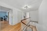 Hardwood flooring throughout, white walls, white doors, and a wood-finish handrail with white balusters