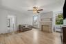 Light wood-finish flooring, stone-clad fireplace with mantel, ceiling fan with integrated lighting, and multiple windows
