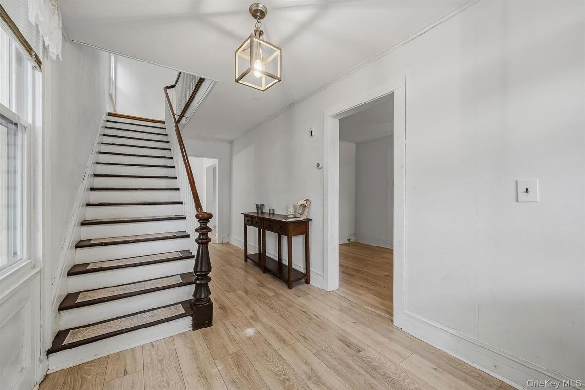 Wood-finish flooring, staircase with dark wood-finish treads and white risers, square caged light fixture, and white wall finishes