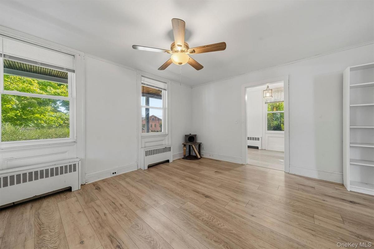 Wood-finish flooring, two windows with blinds, ceiling fan, and built-in shelving