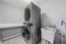 Laundry area featuring a stacked washer and dryer, utility sink with faucet, and light-toned tile flooring