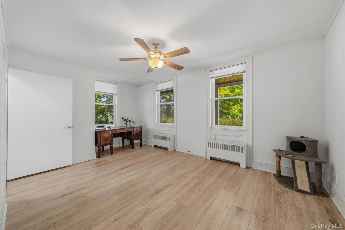 Wood-finish flooring, two windows with roller shades, white walls, and a ceiling fan with integrated lighting