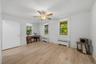 Wood-finish flooring, two windows with roller shades, white walls, and a ceiling fan with integrated lighting
