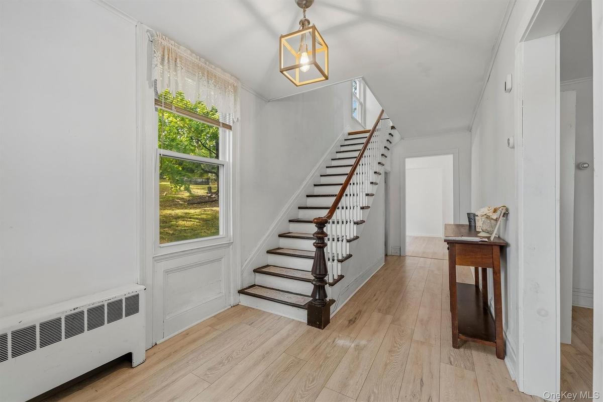 Bright entry hall with staircase, large window, and wood-look flooring.