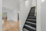 Wood-finish flooring, white wall finishes, dark-painted staircase with textured treads, and multiple doorways
