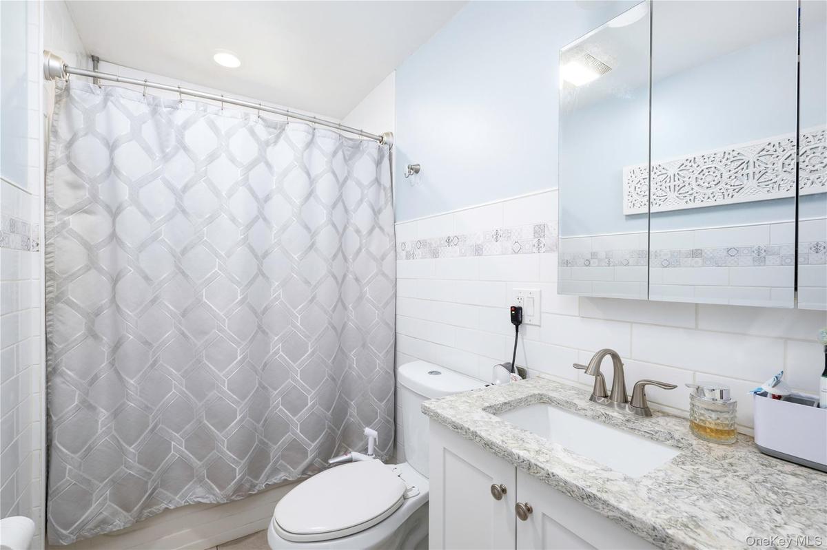 Bathroom featuring a single vanity with a light-toned countertop, white cabinetry, a rectangular undermount sink, and a mirrored medicine cabinet