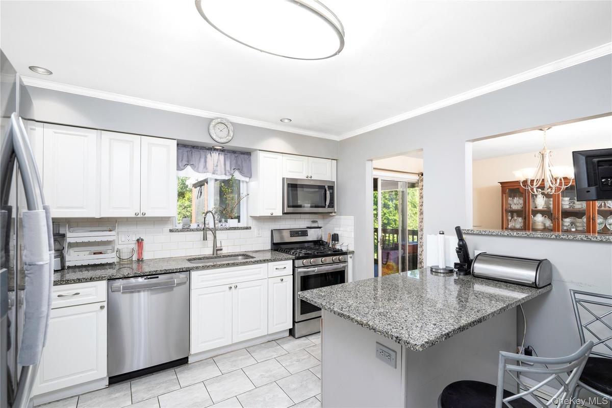 White shaker cabinetry, stainless steel appliances, granite countertops, subway tile backsplash, and tile flooring