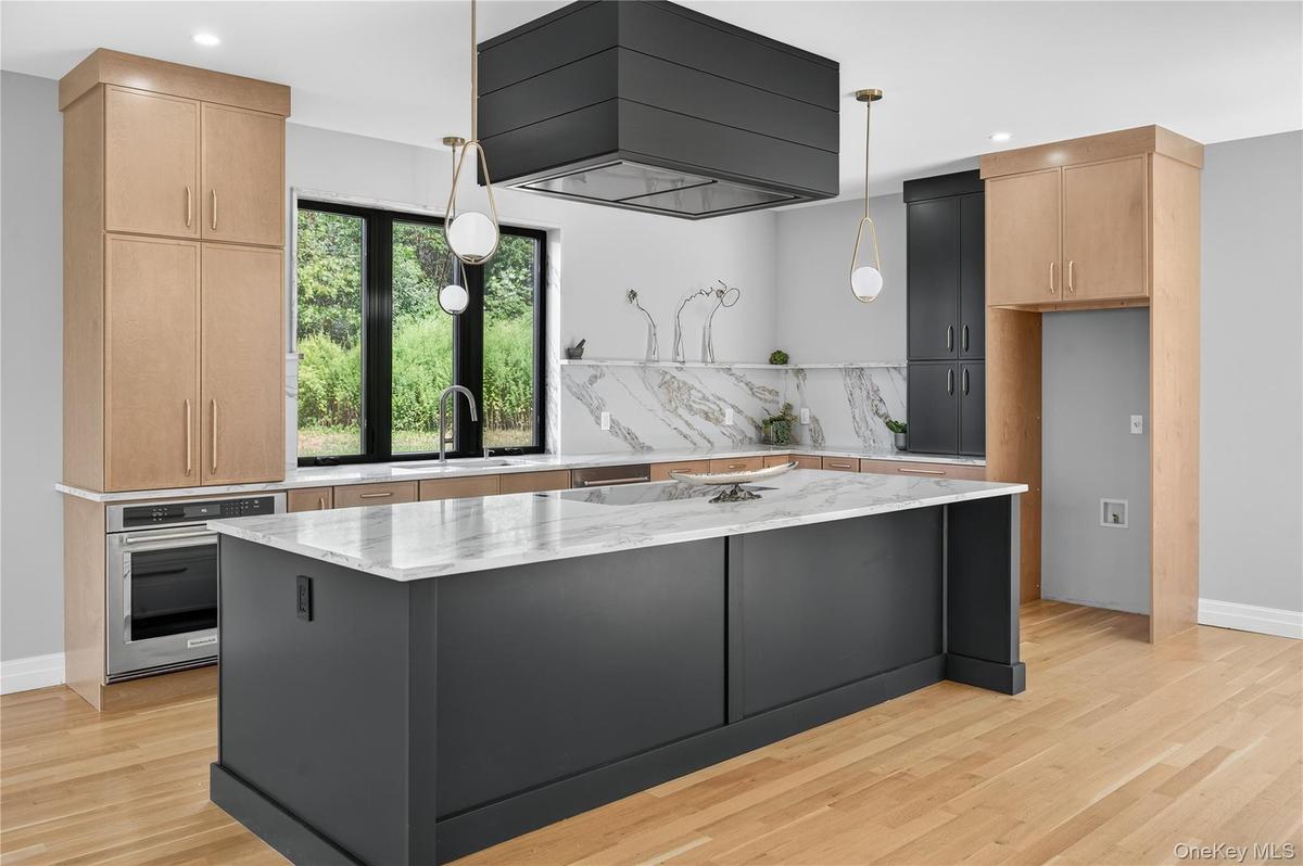 Kitchen featuring light stone countertops, stainless steel oven, decorative light fixtures, wall chimney exhaust hood, and recessed lighting