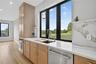 Kitchen with light stone counters, appliances with stainless steel finishes, light wood-style floors, pendant lighting, and light brown cabinetry