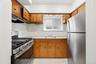 Kitchen featuring wood cabinetry, white tile backsplash, stainless steel range with overhead ventilation, and a stainless steel refrigerator