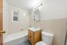 Bathroom featuring a full bathtub, window, vanity with integrated sink, wall-mounted medicine cabinet, and tiled walls